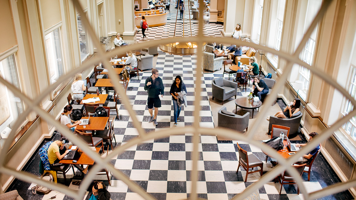 Students sitting at tables and walking down the hall 