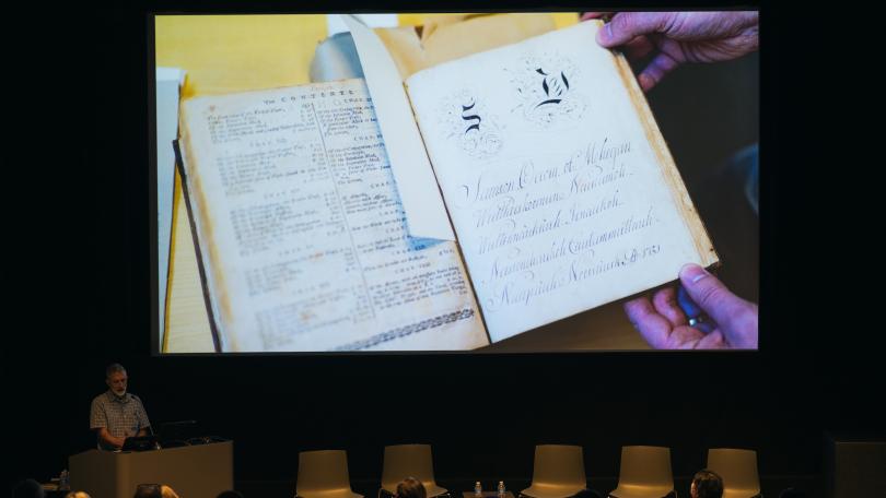 Peter Carini speaks in front of the Advancing Pathways Colloquium with a photo of Samson Occom's papers in the background