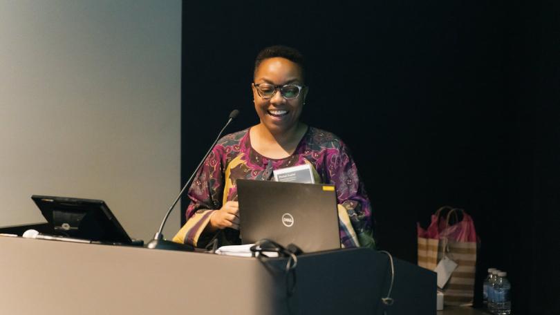 Richel Cuyler, co-organizer of the Advancing Pathways Colloquium stands at a podium smiling