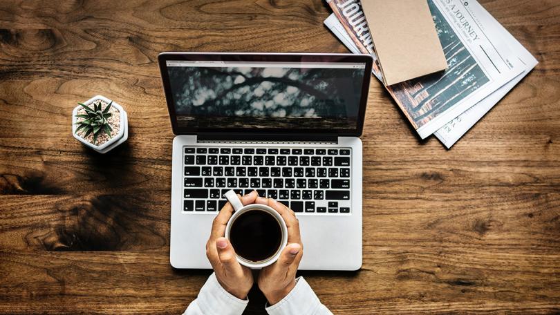 Person holds coffee over laptop