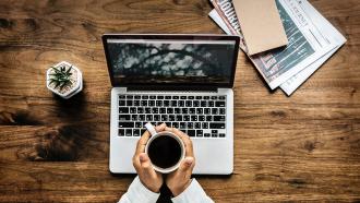 Person holds coffee over laptop