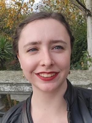A brown haired blue eyed white woman with her hair pulled pack. She is wearing red lipstick and smileing.