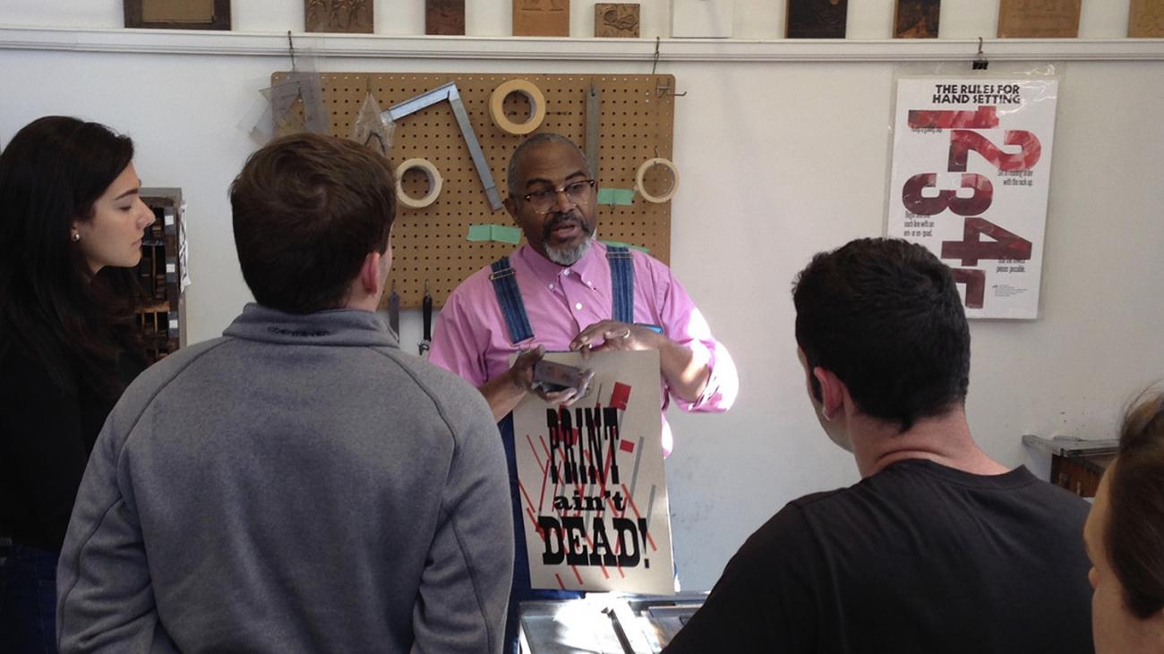 Amos Kennedy talking to students while holding a print that says Print Ain't Dead