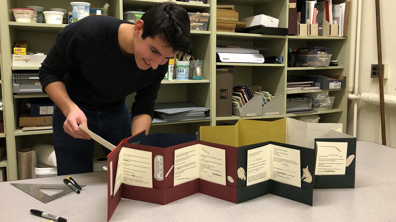Student working on a large accordion book with different colored papers and pockets