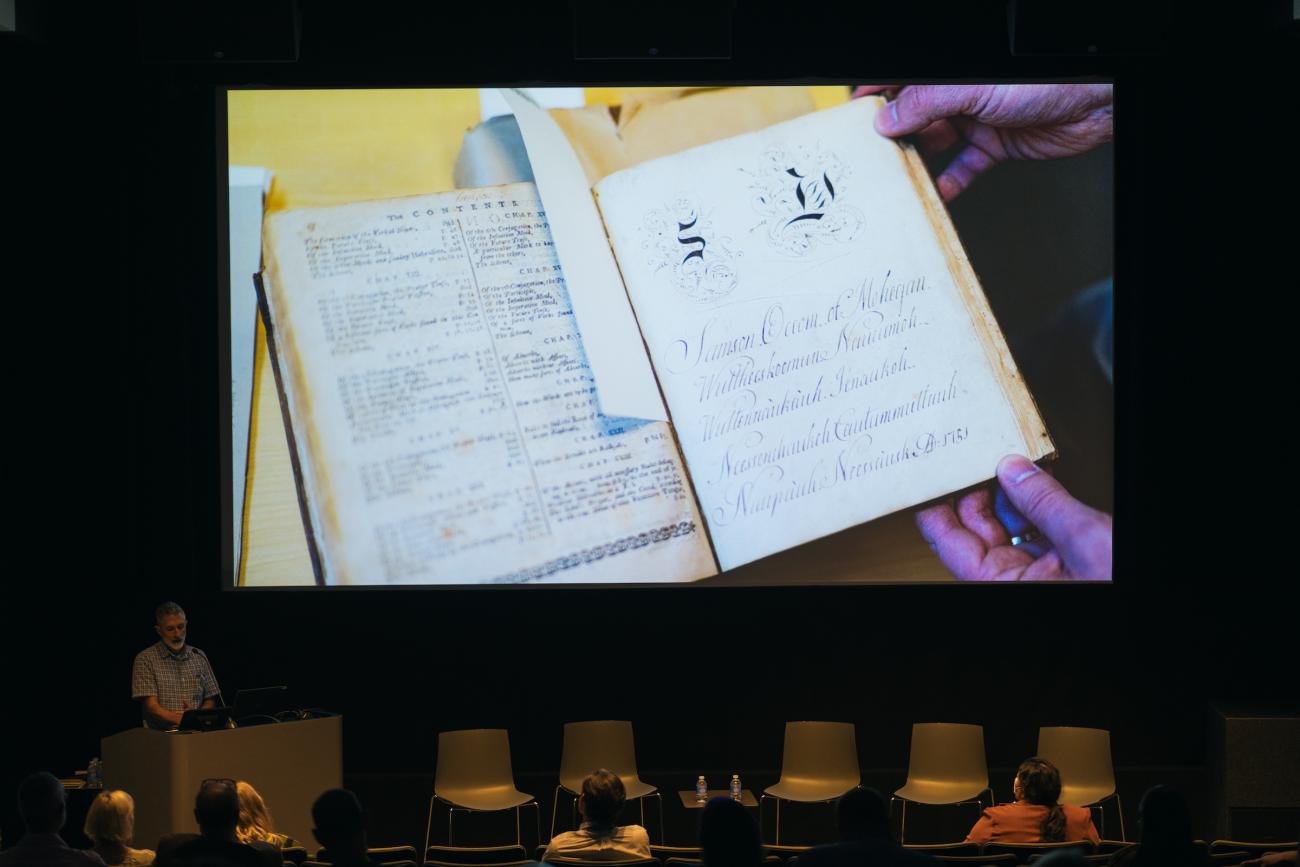 Peter Carini speaks in front of the Advancing Pathways Colloquium with a photo of Samson Occom's papers in the background