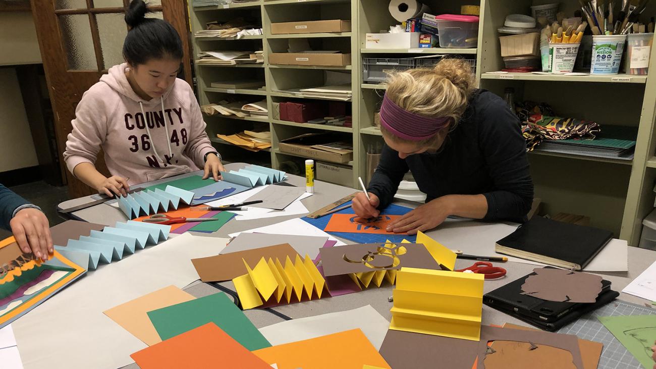 students cutting and gluing paper around a table