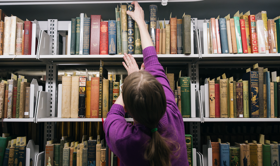librarian pulls a book from the packed shelves of Rauner Library