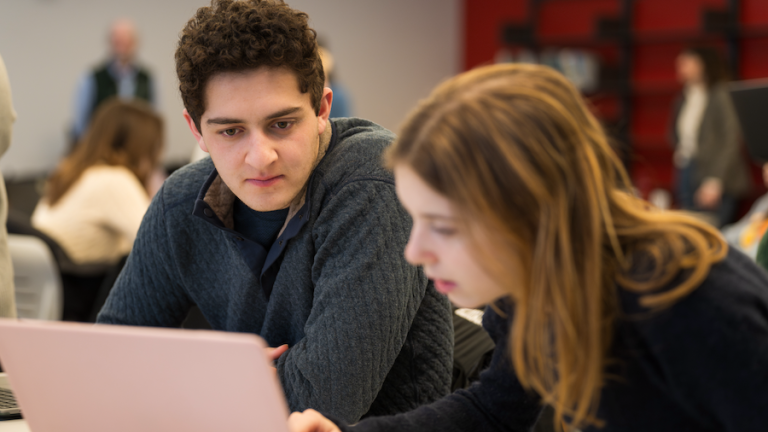 two students collaborate on their laptops