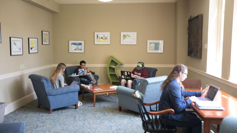 Four people sitting in chairs and studying. Various framed pieces of art hangs on the walls.